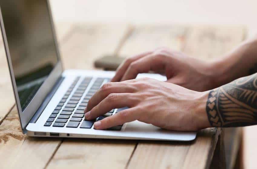 Close up image of tattooed hands using computer